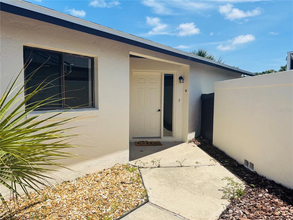 A beige exterior wall features a white front door, a window, and a concrete walkway — 79 CLUB HOUSE DRIVE, PALM COAST, FL