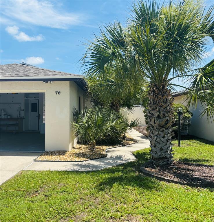 A view of a house exterior featuring a garage, a walkway, and palm trees — 79 CLUB HOUSE DRIVE, PALM COAST, FL