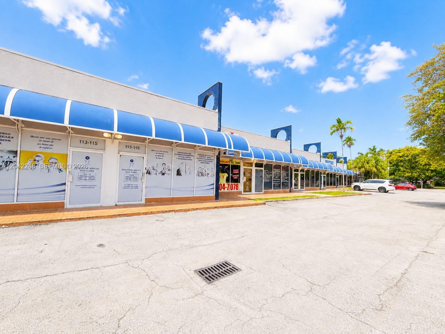 A single-story commercial strip mall features blue awnings over glass storefronts and a parking lot — 10240 SW 56th St # C, Miami FL 33165, MIAMI, FL