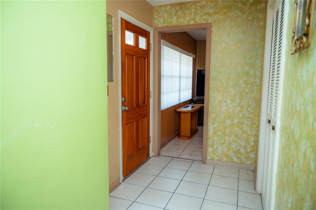 A tiled entryway features a wooden front door, yellow wallpaper, and a doorway to another room — 2705 SHERINGHAM ROAD UNIT 6, ORLANDO, FL