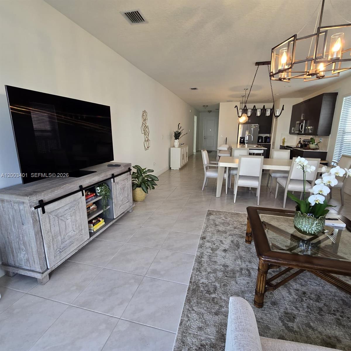 A living room and dining area feature tile flooring, a large television, and modern lighting — 5615 CARRARA DR, Ave Maria FL 34142, AVE MARIA, FL