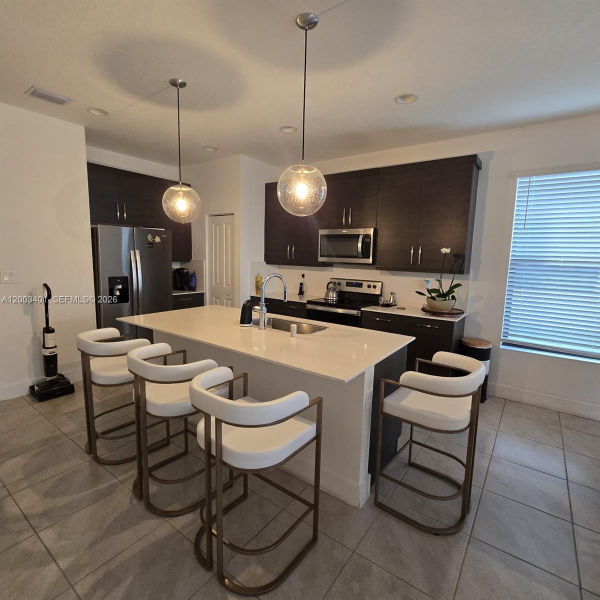 A modern kitchen features dark cabinetry, a white quartz island, and four bar stools — 5615 CARRARA DR, Ave Maria FL 34142, AVE MARIA, FL