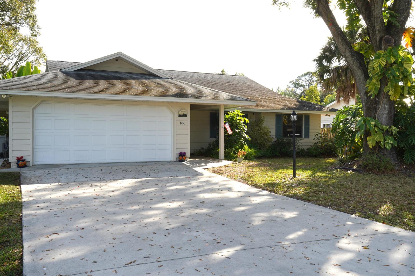 A single-story house with a white garage door, beige siding, and a concrete driveway — 166 23rd Avenue, Vero Beach FL 32962, VERO BEACH, FL