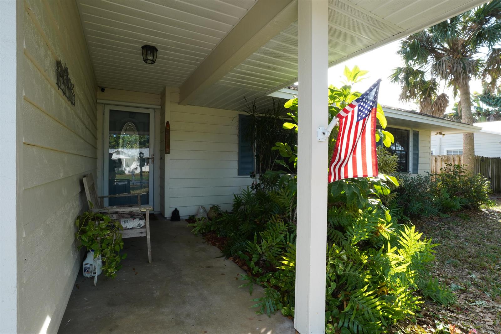 A covered front porch features a wooden bench, a hanging American flag, and lush landscaping — 166 23rd Avenue, Vero Beach FL 32962, VERO BEACH, FL