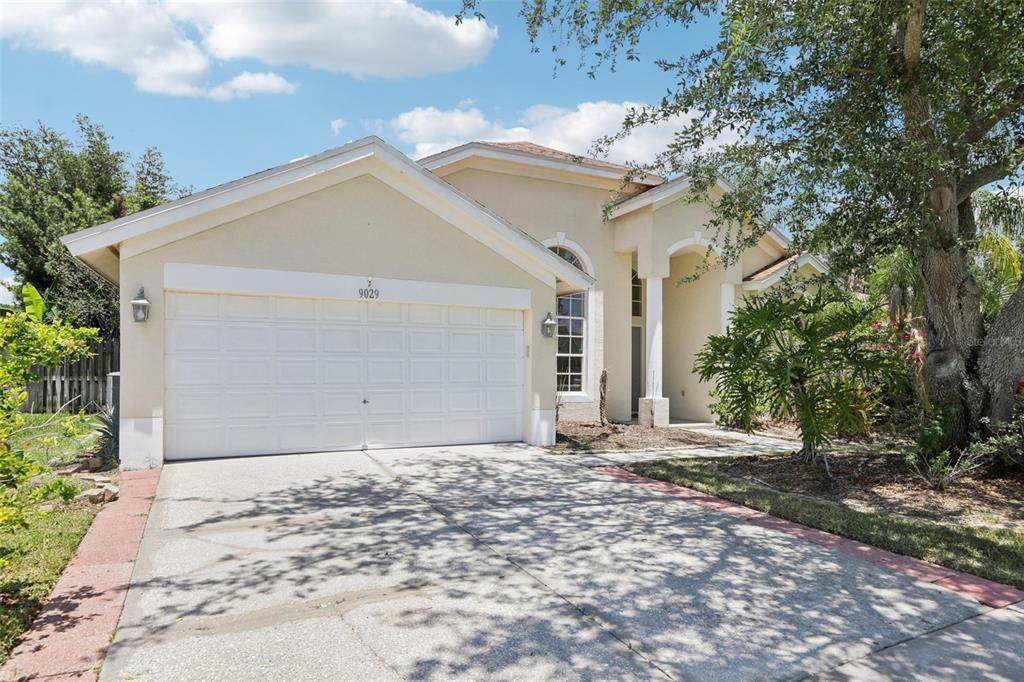 A single-story house with a white garage door, beige stucco exterior, and a concrete driveway — 9029 WESTBAY BOULEVARD, TAMPA, FL