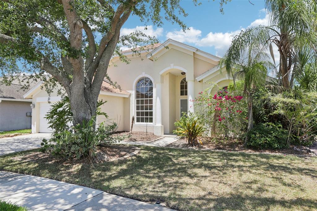 A single-story beige house with a large arched window, a two-car garage, and mature landscaping — 9029 WESTBAY BOULEVARD, TAMPA, FL