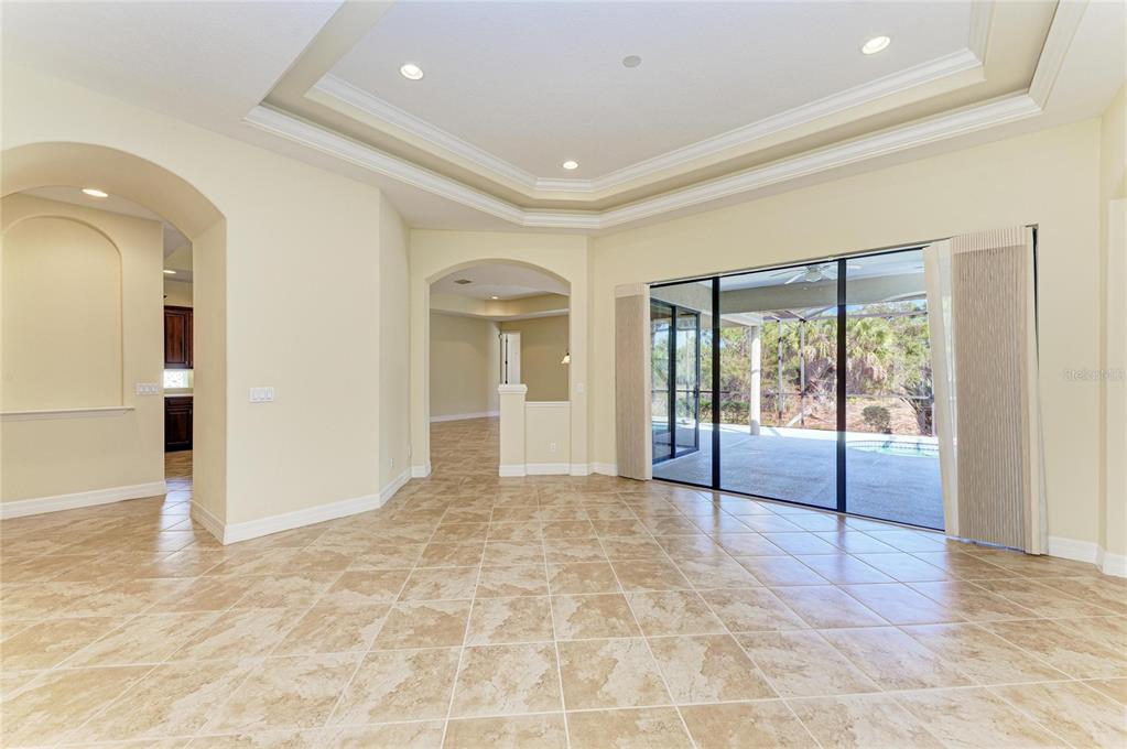 A spacious living room features tile flooring, a tray ceiling, and sliding glass doors to a pool — 650 CRANE PRAIRIE WAY, OSPREY, FL