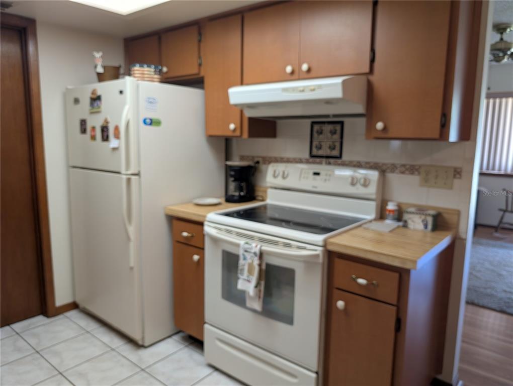 A kitchen features white appliances, wood-toned cabinets, a tiled floor, and a laminate countertop — 8483 SW 106TH PLACE, OCALA, FL