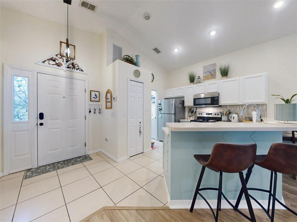 An open-concept kitchen with light blue cabinets and tile flooring flows into a living area — 242 PINE BLUFF AVENUE UNIT 242, DELAND, FL