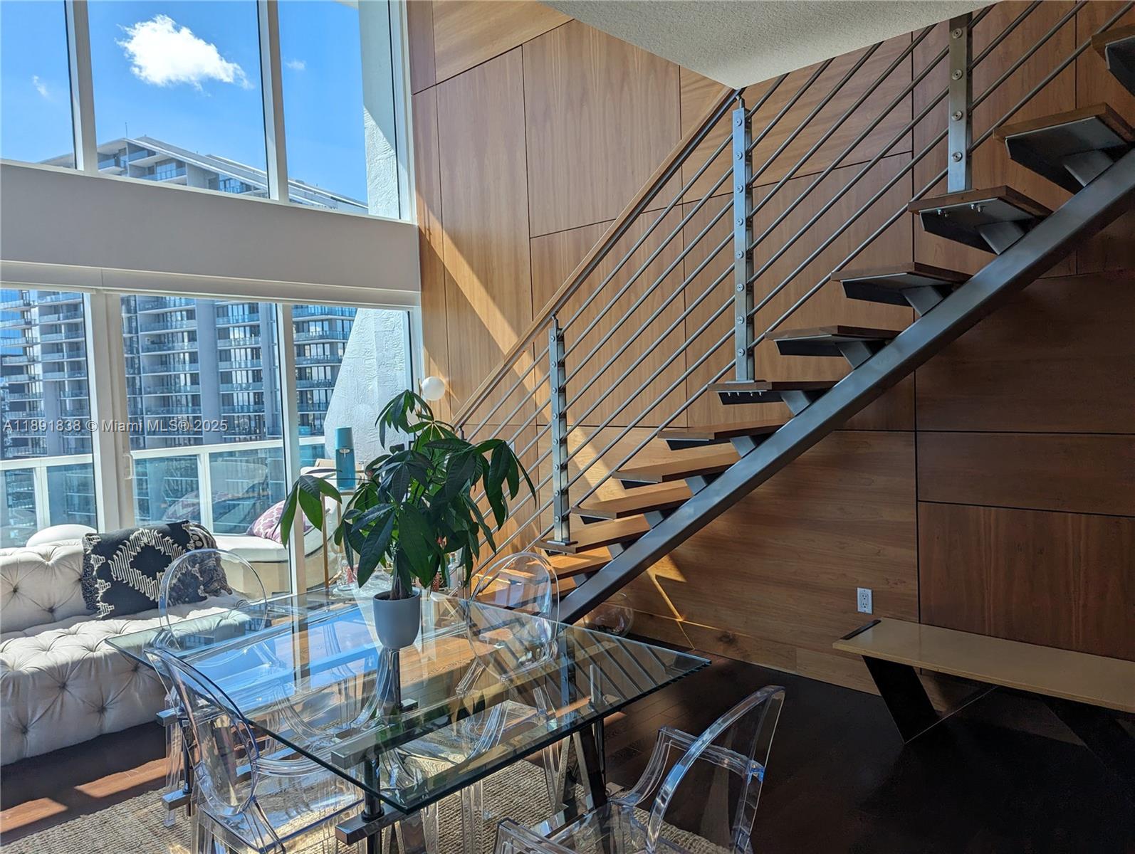 A dining area features a glass table, transparent chairs, and a modern floating staircase — 41 SE 5th St # 2302, Miami FL 33131, MIAMI, FL