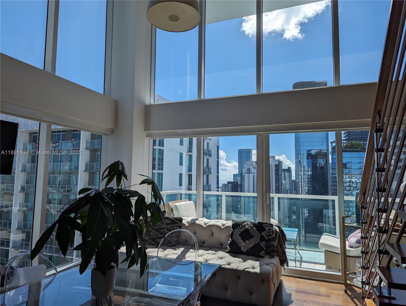 A living room features floor-to-ceiling windows, a tufted sofa, and a view of city skyscrapers — 41 SE 5th St # 2302, Miami FL 33131, MIAMI, FL