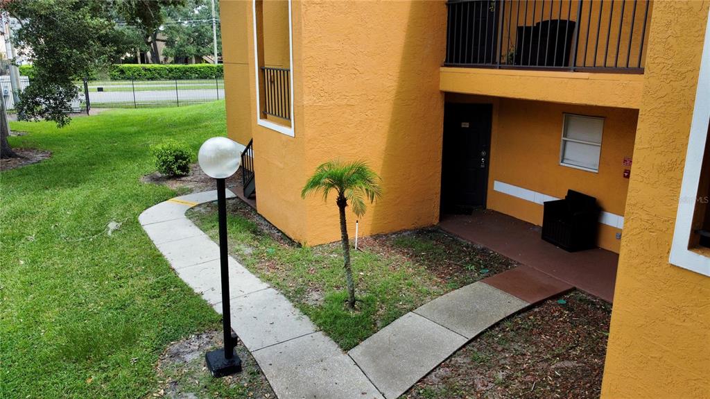 An exterior view of a yellow apartment building with a walkway, palm tree, and balcony — 4548 COMMANDER DRIVE UNIT 1412, ORLANDO, FL