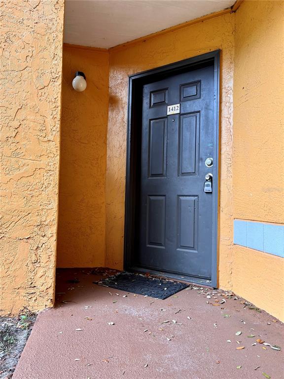 A dark-colored front door with the number 1412 is set into a textured orange wall — 4548 COMMANDER DRIVE UNIT 1412, ORLANDO, FL