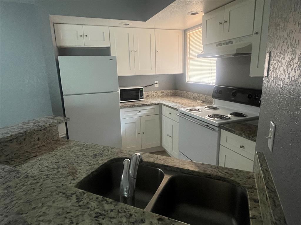 A kitchen features white cabinets, granite countertops, a double sink, and white appliances — 4548 COMMANDER DRIVE UNIT 1412, ORLANDO, FL