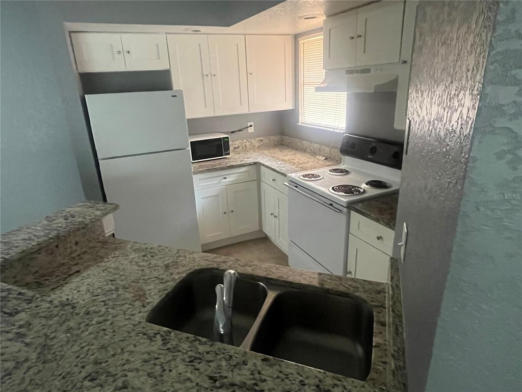 A kitchen features white cabinets, granite countertops, a double sink, and white appliances — 4548 COMMANDER DRIVE UNIT 1412, ORLANDO, FL