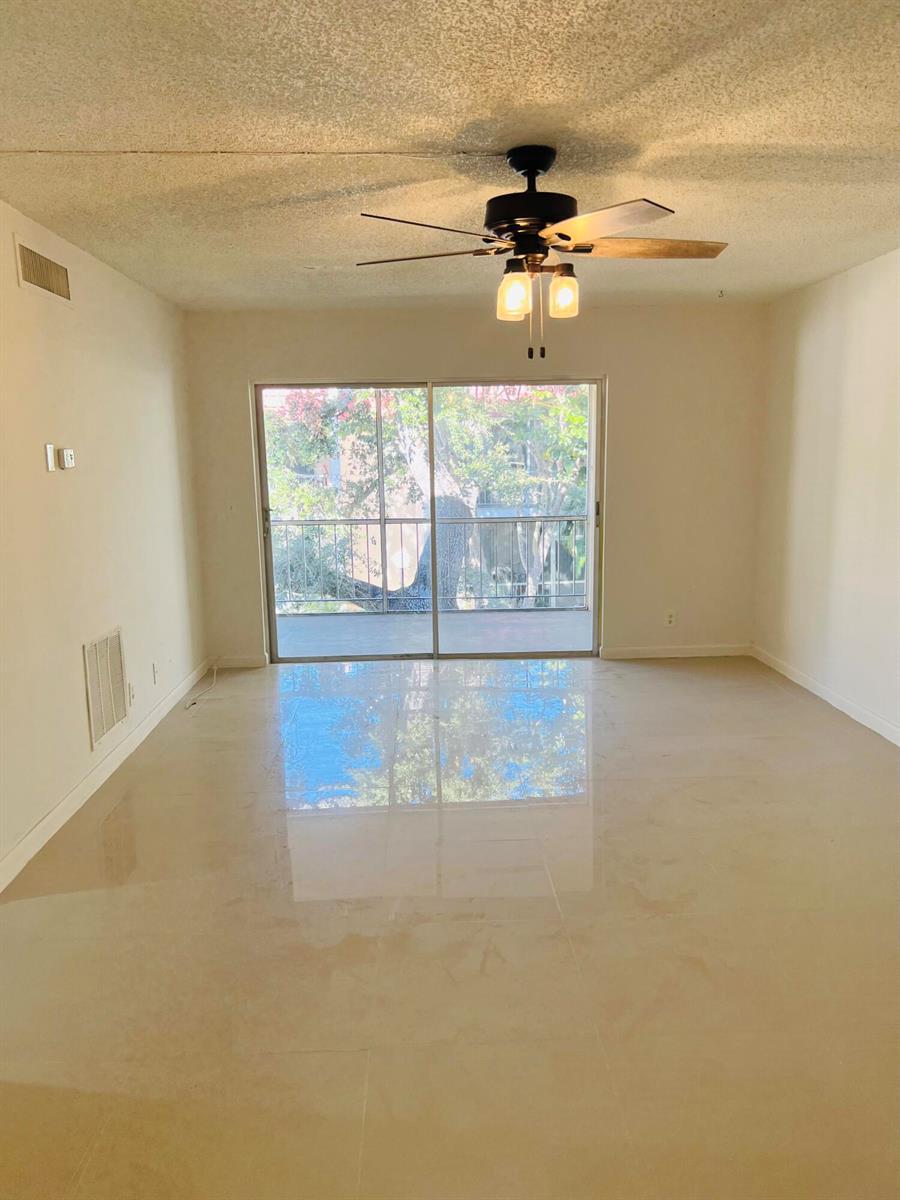 An empty living room with light-colored tile flooring, a ceiling fan, and a sliding glass door — 614 NW 13th Street # 0280, Boca Raton FL 33486, BOCA RATON, FL