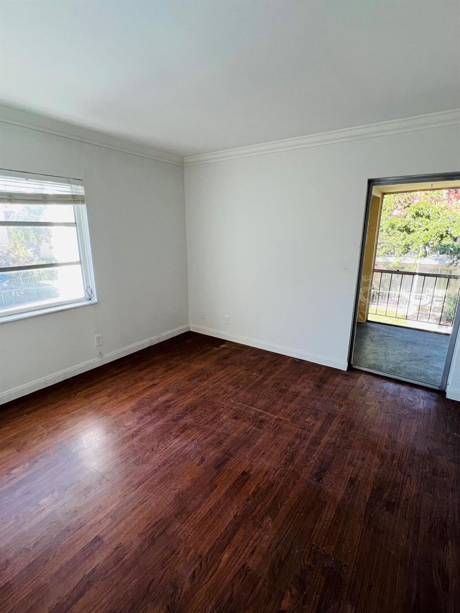 An empty room with dark wood-look flooring, white walls, a window, and a balcony door — 614 NW 13th Street # 0280, Boca Raton FL 33486, BOCA RATON, FL