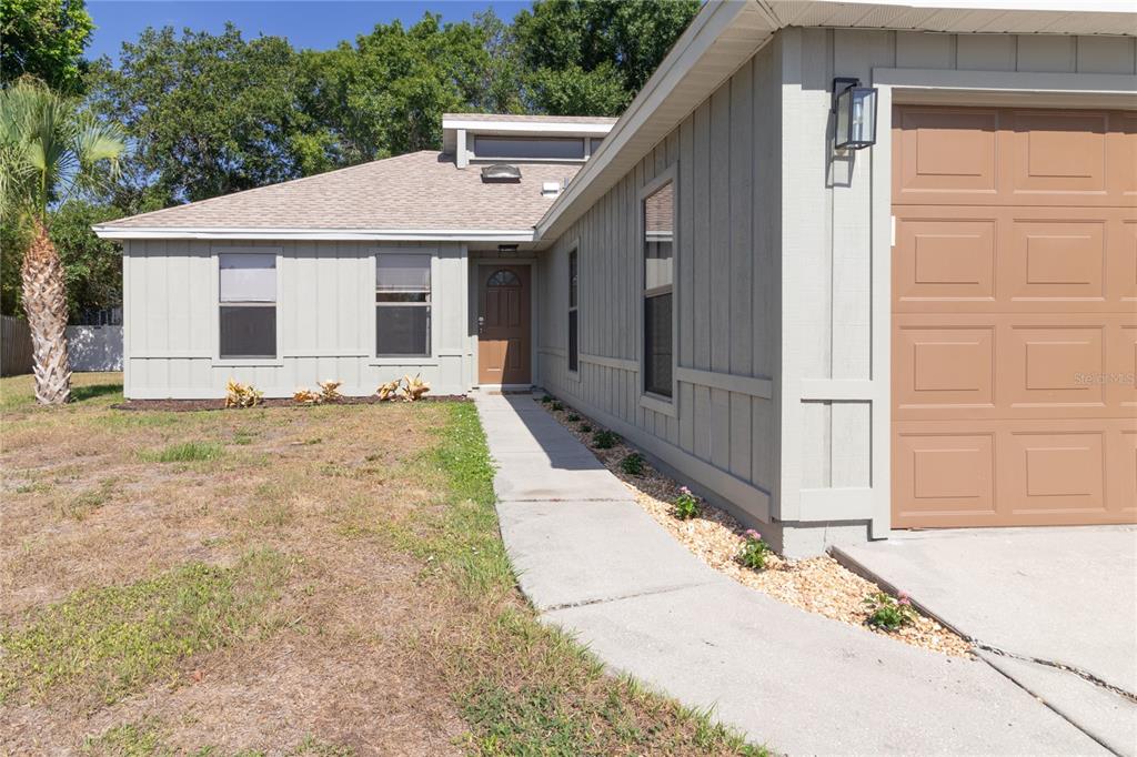 The exterior of a single-story house features light gray siding, a brown garage door, and a walkway — 8232 COUNTRY OAKS COURT, SARASOTA, FL