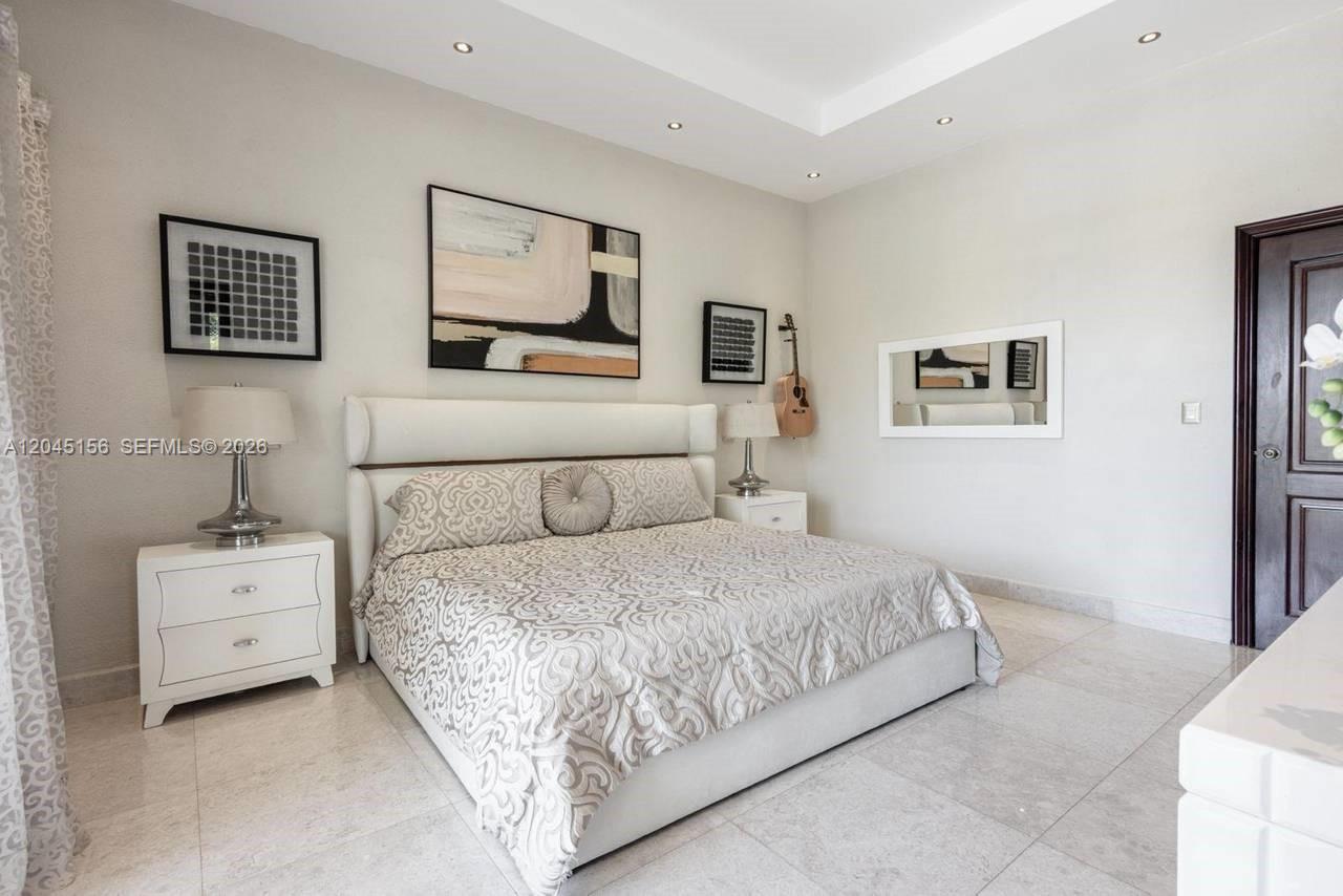 A bedroom features a white upholstered bed, two nightstands, wall art, and tile flooring — 0 cocotal, FL