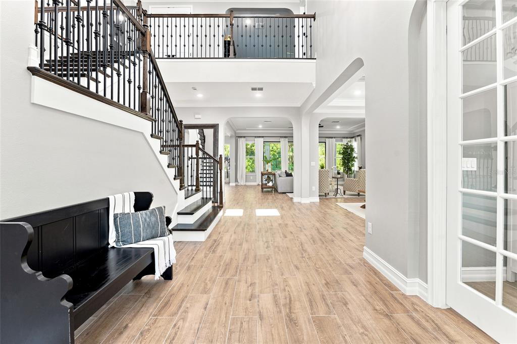 A bright foyer features wood-look tile flooring, a black staircase, and a black wooden bench — 29818 PICANA LANE, WESLEY CHAPEL, FL