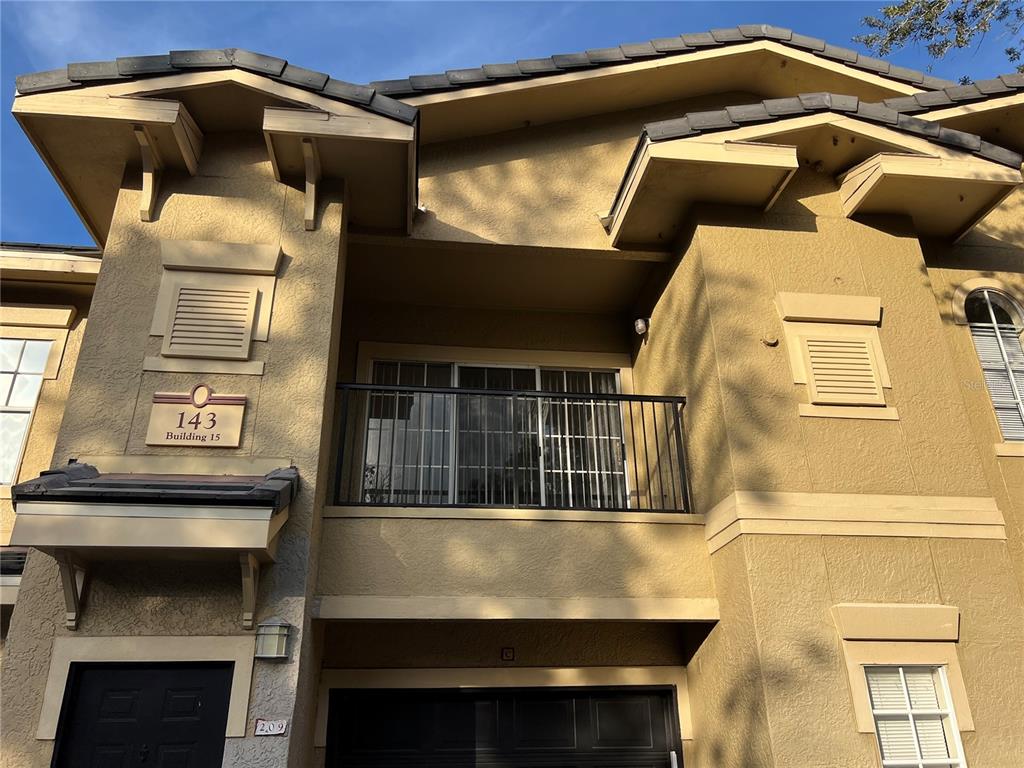 A two-story tan stucco building exterior features a balcony, a garage, and a building number — 143 VILLA DI ESTE TERRACE UNIT 209, LAKE MARY, FL