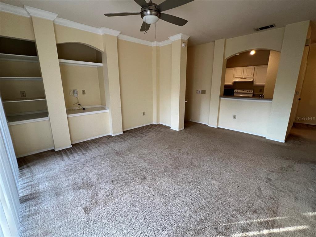 A carpeted living room features a built-in shelving unit, an arched alcove, and a ceiling fan — 143 VILLA DI ESTE TERRACE UNIT 209, LAKE MARY, FL