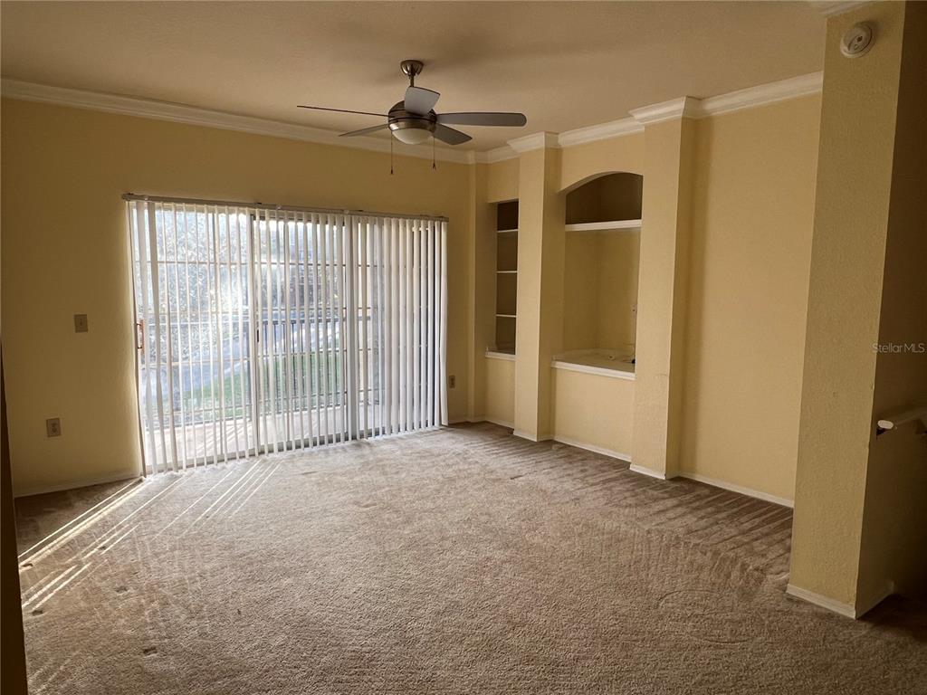 A living room with beige carpet, yellow walls, a ceiling fan, and sliding glass doors — 143 VILLA DI ESTE TERRACE UNIT 209, LAKE MARY, FL