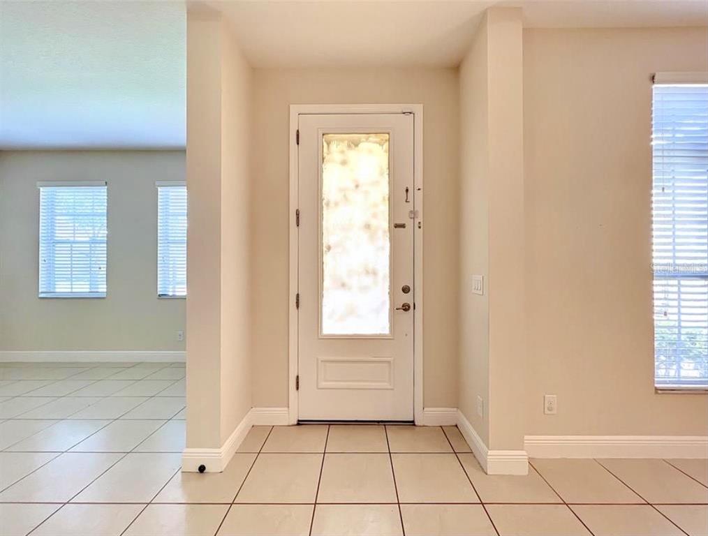 An entryway with light-colored tile flooring, a white front door, and windows with blinds — 14517 BLACK LAKE PRESERVE STREET, WINTER GARDEN, FL