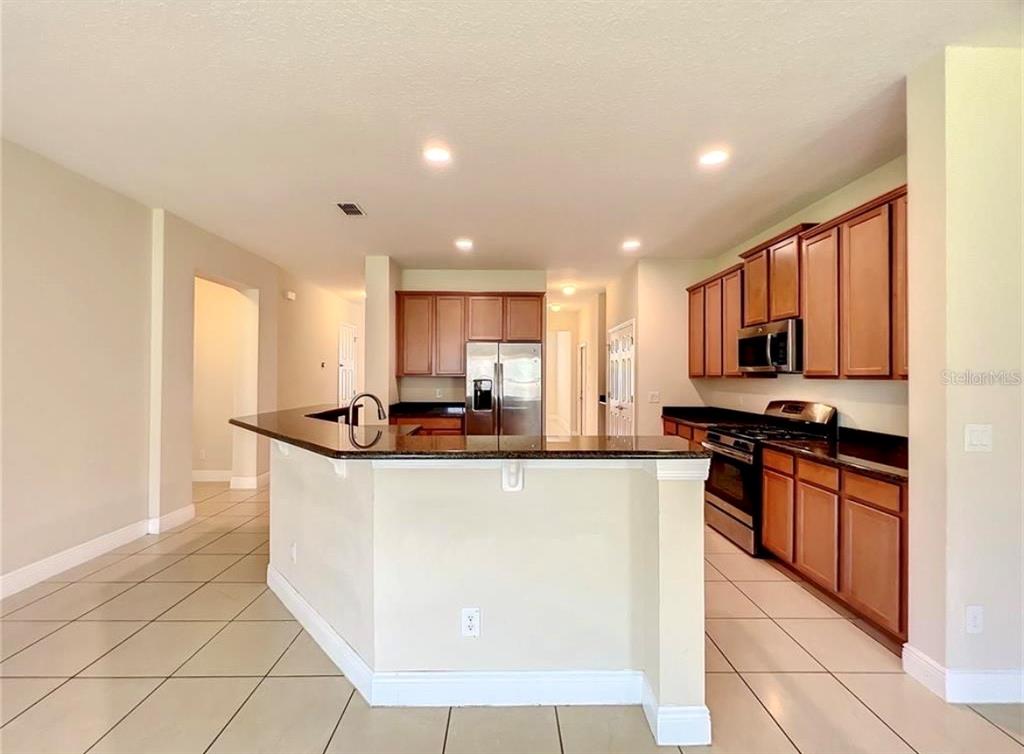 A kitchen features wood cabinets, dark countertops, stainless steel appliances, and tile flooring — 14517 BLACK LAKE PRESERVE STREET, WINTER GARDEN, FL