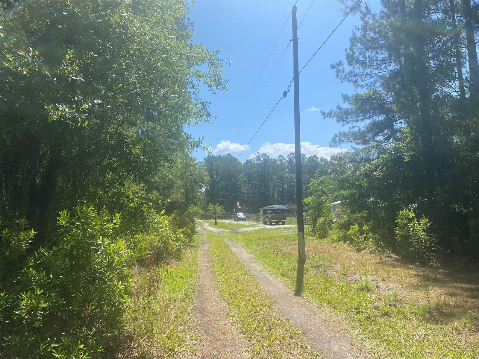 A dirt driveway leads toward a house and vehicles surrounded by trees and a utility pole — Tbd NE 155 Lane, FL 32134, FL