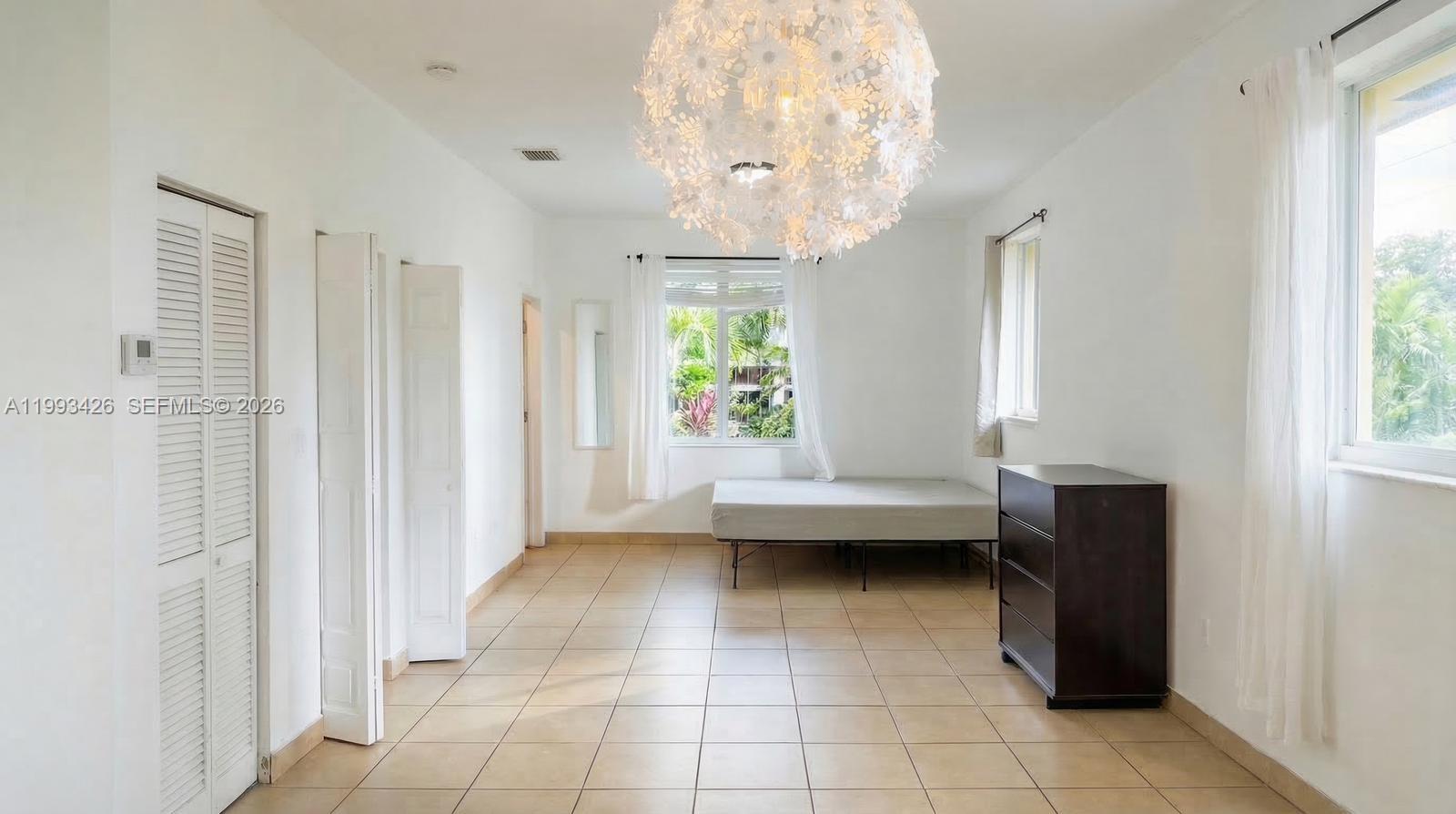A bedroom with white walls, tile flooring, a large floral chandelier, and a bed frame — 404 NE 27th St, Miami FL 33137, MIAMI, FL