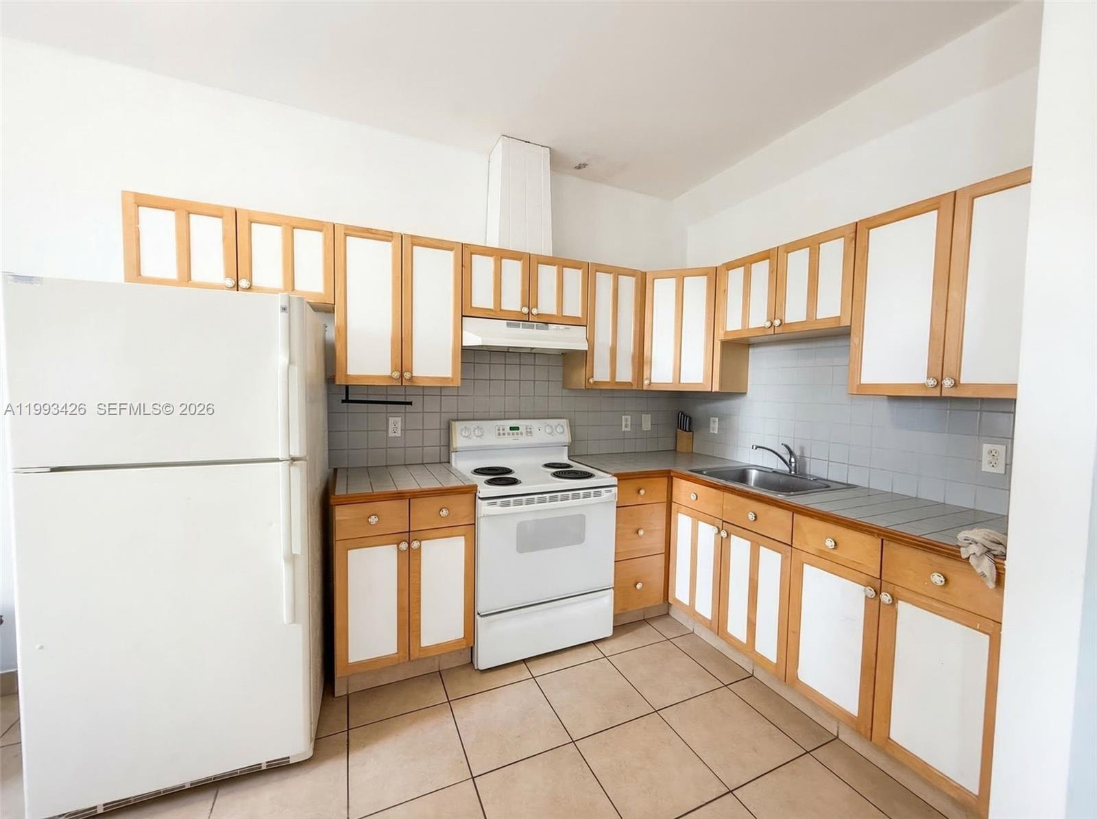 A kitchen features white appliances, light wood-trimmed cabinets, gray tiled backsplashes, and beige floor tiles — 404 NE 27th St, Miami FL 33137, MIAMI, FL