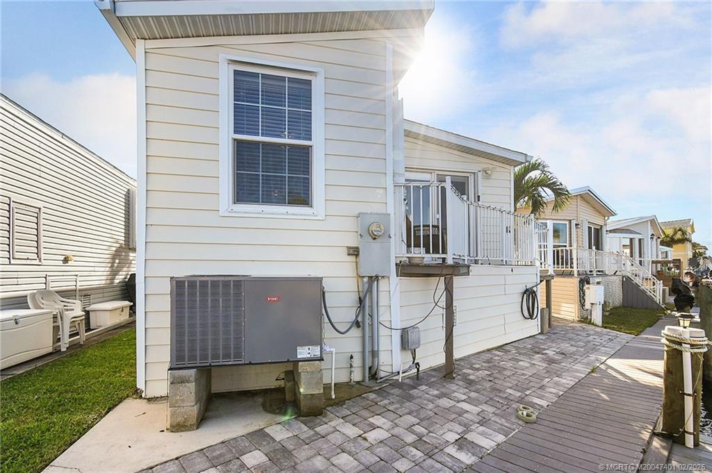 The exterior of a light-colored mobile home features a central air conditioning unit and deck — 1092 Nettles Boulevard, Jensen Beach FL 34957, JENSEN BEACH, FL