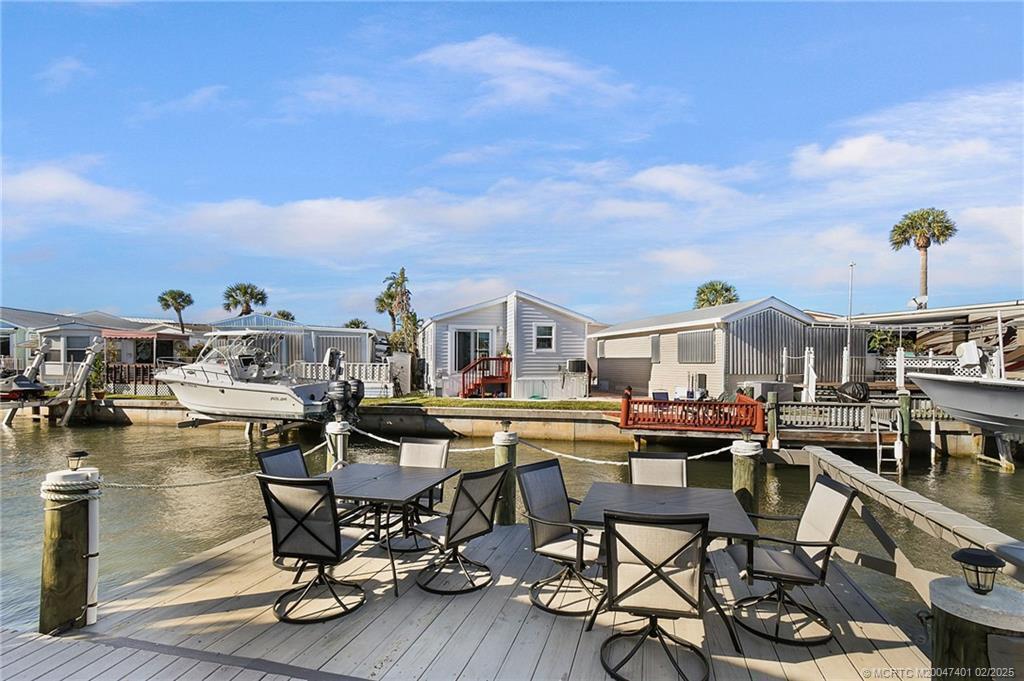 A wooden deck features two dining sets overlooking a canal with docked boats and homes — 1092 Nettles Boulevard, Jensen Beach FL 34957, JENSEN BEACH, FL