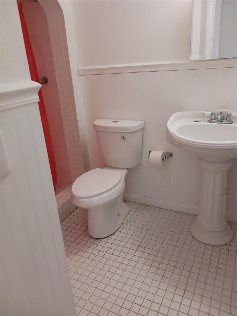 A bathroom features a white pedestal sink, a toilet, and a shower with a red curtain — 7605 W Atlantic Boulevard # 106, Margate FL 33063, MARGATE, FL