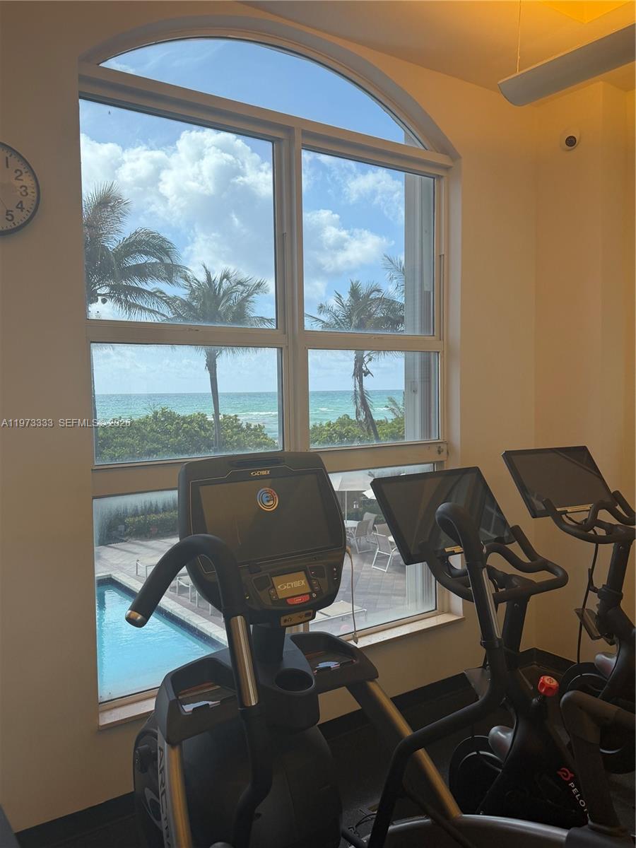 A gym features exercise equipment facing a large arched window with a view of the ocean — 2080 S Ocean Dr # 308, Hallandale Beach FL 33009, HALLANDALE BEACH, FL