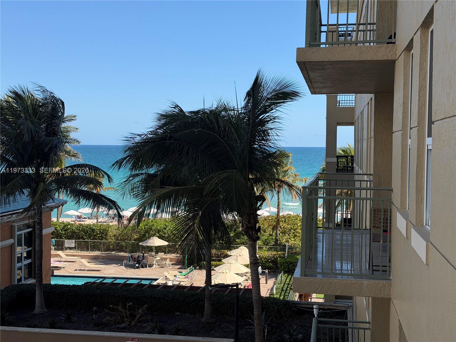 A view from a balcony overlooking a swimming pool, palm trees, and the ocean — 2080 S Ocean Dr # 308, Hallandale Beach FL 33009, HALLANDALE BEACH, FL