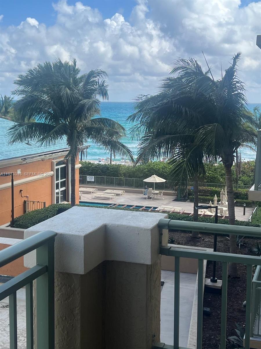 A balcony view overlooks a swimming pool, palm trees, and the ocean — 2080 S Ocean Dr # 308, Hallandale Beach FL 33009, HALLANDALE BEACH, FL