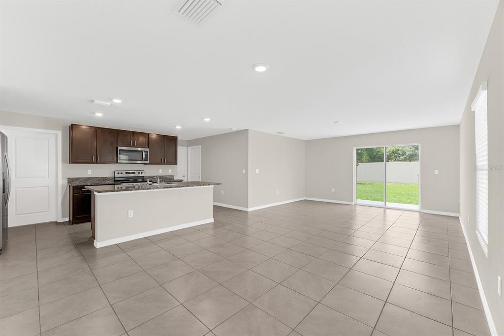 An open-concept kitchen and living area with tile flooring, dark wood cabinets, and sliding doors — 12153 DOWNY BIRCH DRIVE, RIVERVIEW, FL