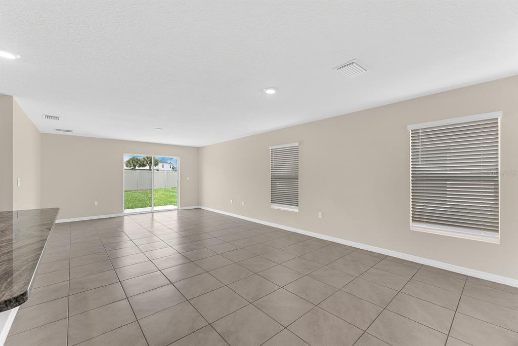 An empty room with beige walls, tile flooring, large windows, and a sliding glass door — 12153 DOWNY BIRCH DRIVE, RIVERVIEW, FL
