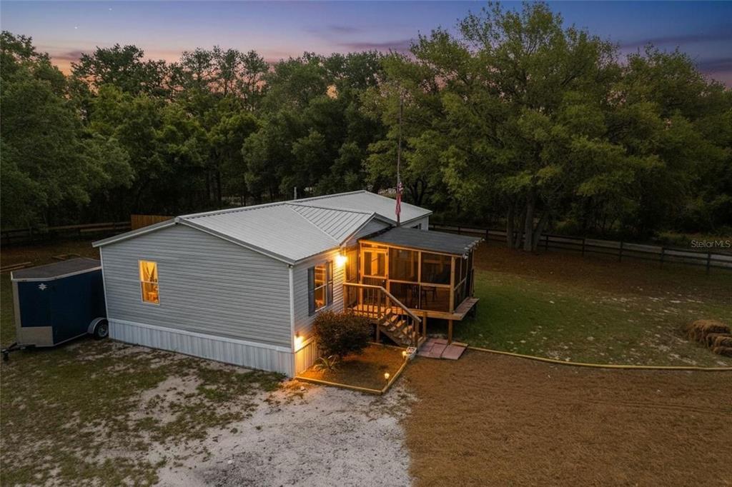 An elevated exterior view of a single-story manufactured home with a screened-in porch at dusk — 7360 SW 157TH LANE, DUNNELLON, FL