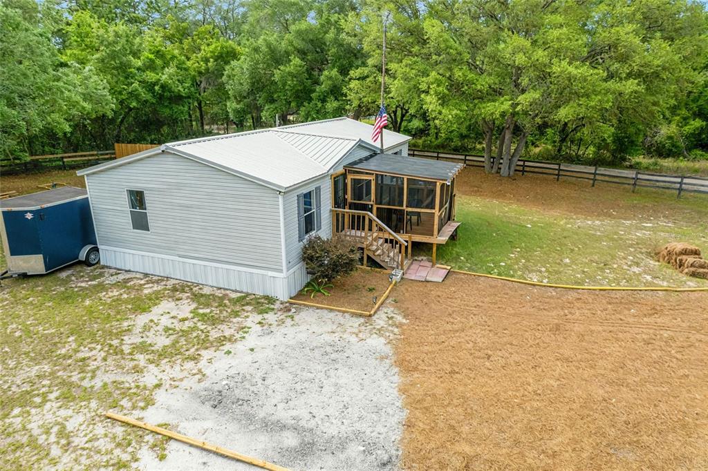 An elevated view of a light-colored manufactured home with a screened porch and metal roof — 7360 SW 157TH LANE, DUNNELLON, FL