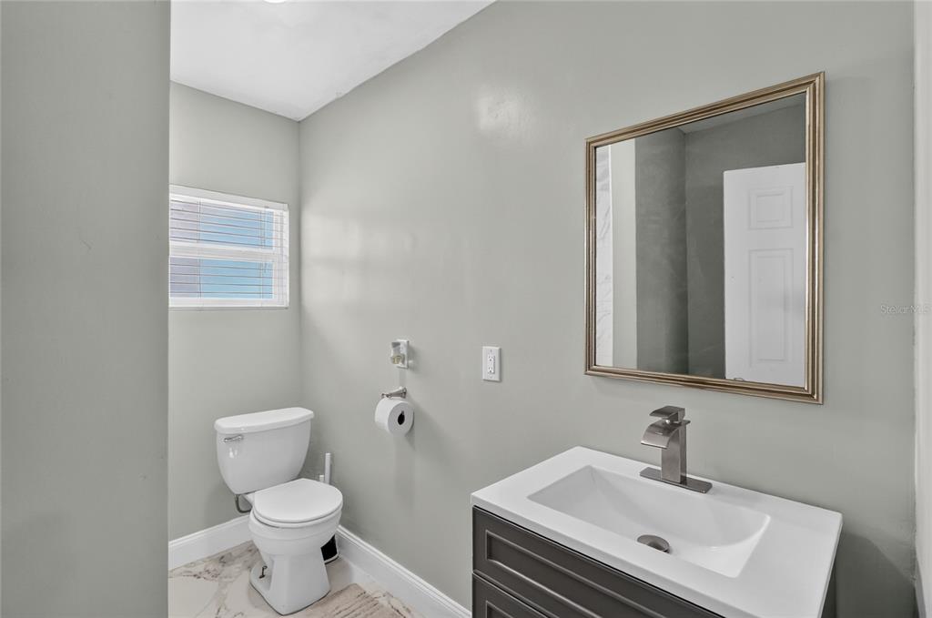 A bathroom features a white toilet, a dark gray vanity with a sink, and a mirror — 1119 54TH AVENUE N, ST PETERSBURG, FL