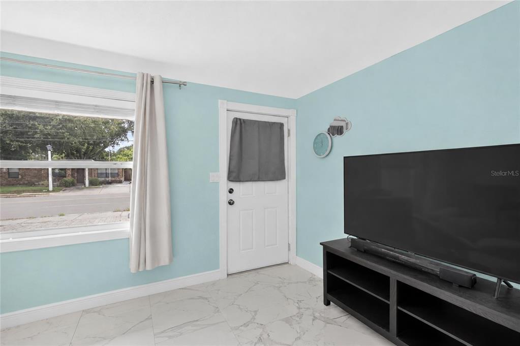 A living room features light blue walls, white tile flooring, a window, and a television — 1119 54TH AVENUE N, ST PETERSBURG, FL