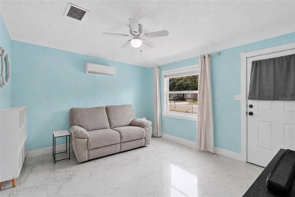 A living room features light blue walls, a gray sofa, and white marble-look tile flooring — 1119 54TH AVENUE N, ST PETERSBURG, FL