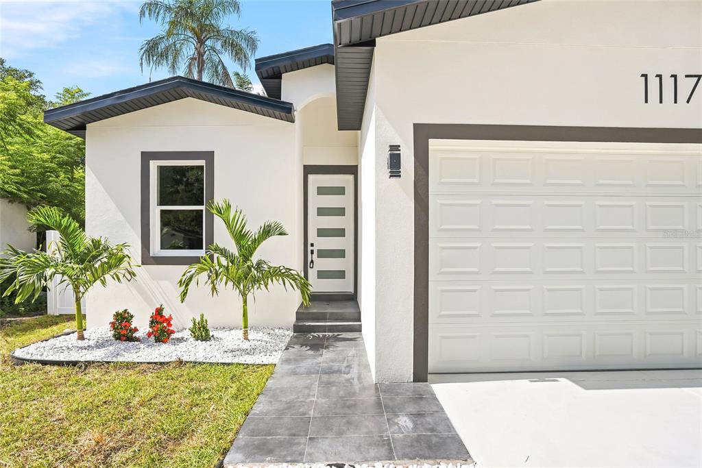 The exterior of a white house features a dark-framed door, garage, and tiled walkway — 1117 15TH AVENUE NW, LARGO, FL