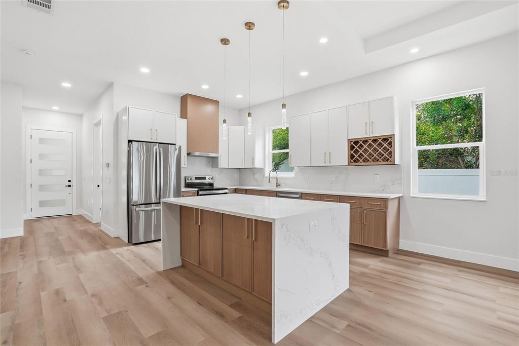A modern kitchen features white upper cabinets, wood lower cabinets, a quartz island, and stainless appliances — 1117 15TH AVENUE NW, LARGO, FL