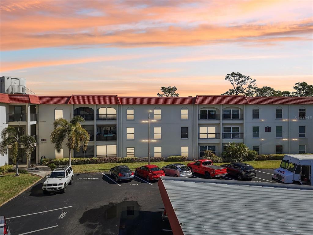An exterior view of a multi-story apartment building with a parking lot in front — 2700 BAYSHORE BOULEVARD UNIT 1305, DUNEDIN, FL
