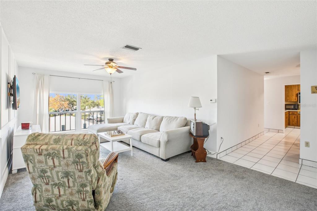 A living room features a beige sectional, a patterned armchair, and a tiled entryway — 2700 BAYSHORE BOULEVARD UNIT 1305, DUNEDIN, FL