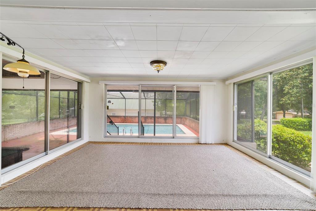 A sunroom with a large area rug, tile ceiling, and sliding glass doors overlooking a pool — 530 N RIDGE AVENUE, LAKE ALFRED, FL